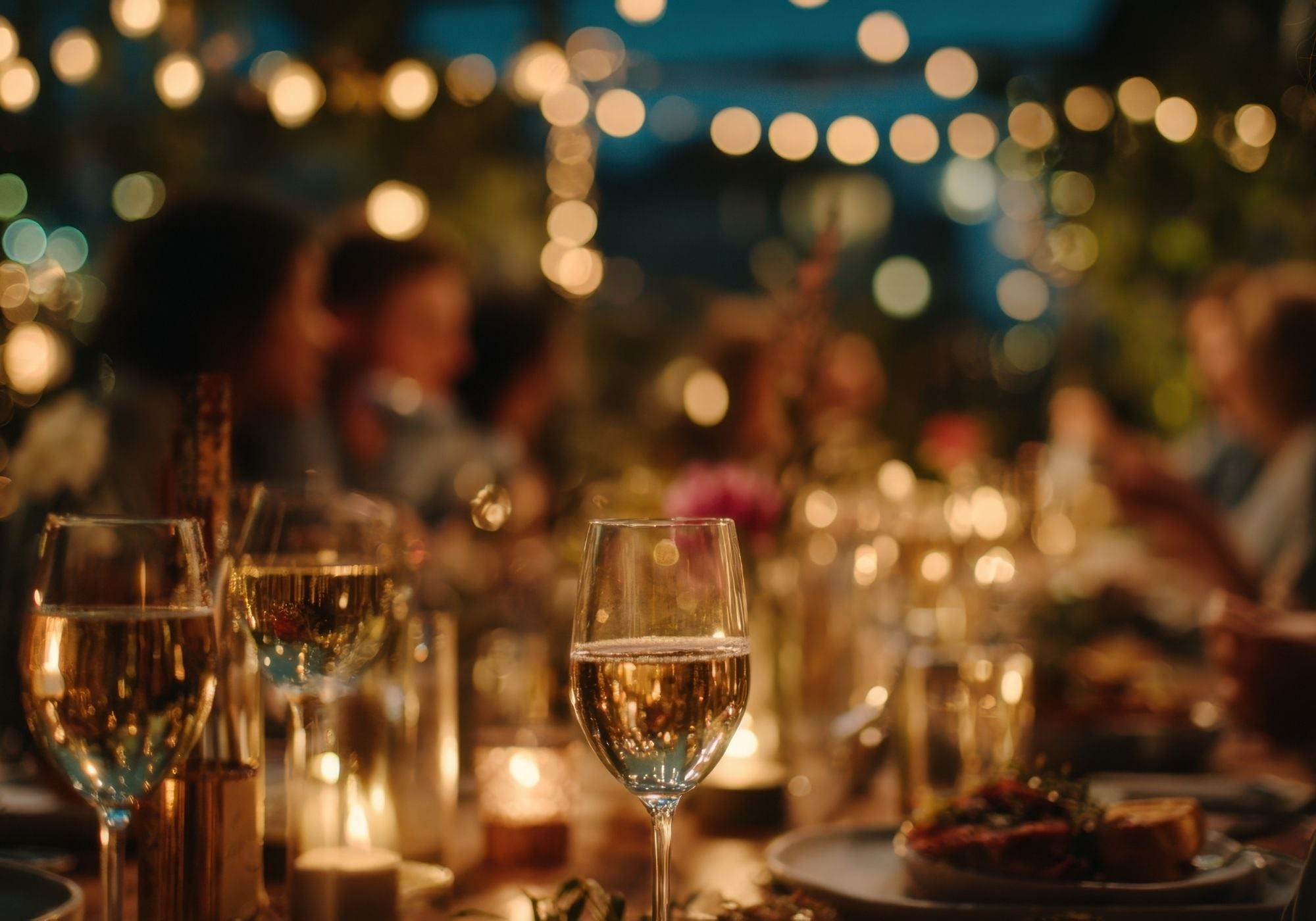 Glas goldener Dessertwein auf einem warm beleuchteten Abendtisch mit Kerzen und weichen Lichtreflexen.